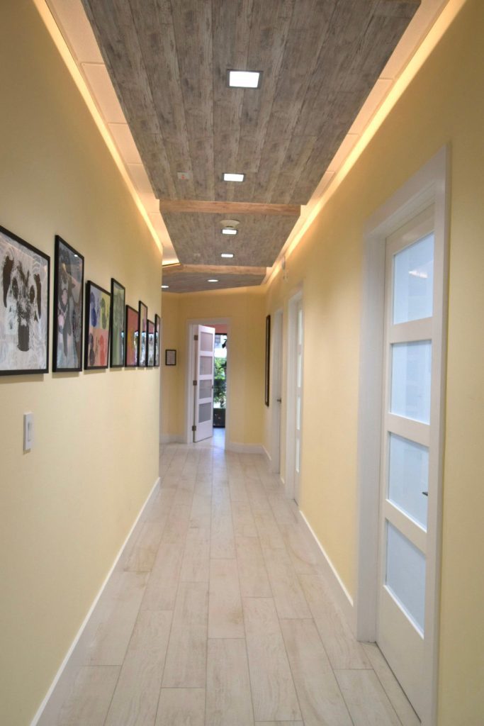 indirect lighting in corridor with cypress wood ceiling and wood look plank tile floors. doors with glass panels