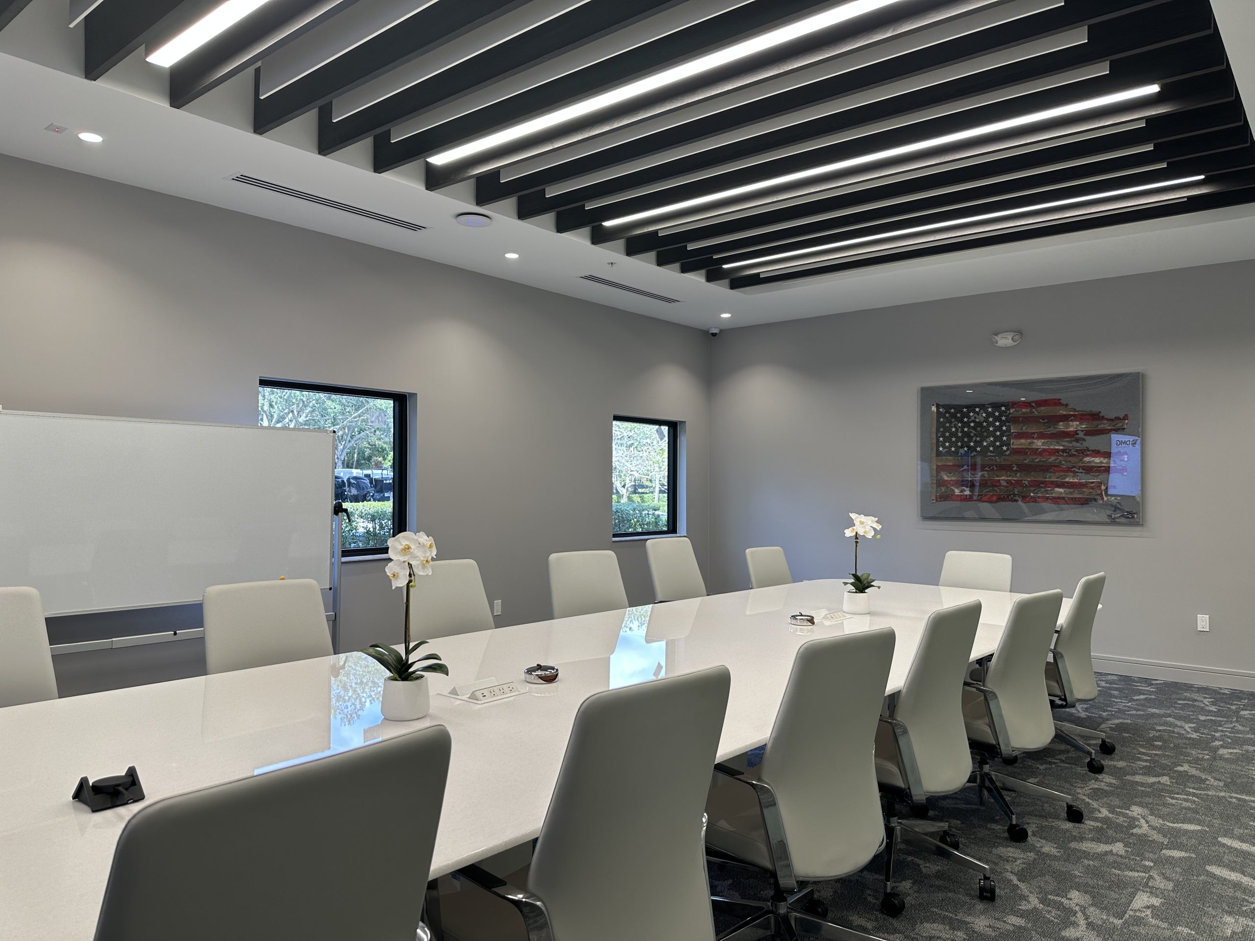 White marble top twenty feet long by six feet wide, grey leather chairs, grey carpet tile floor, wood-stained beams and pendant led fixtures in ceiling